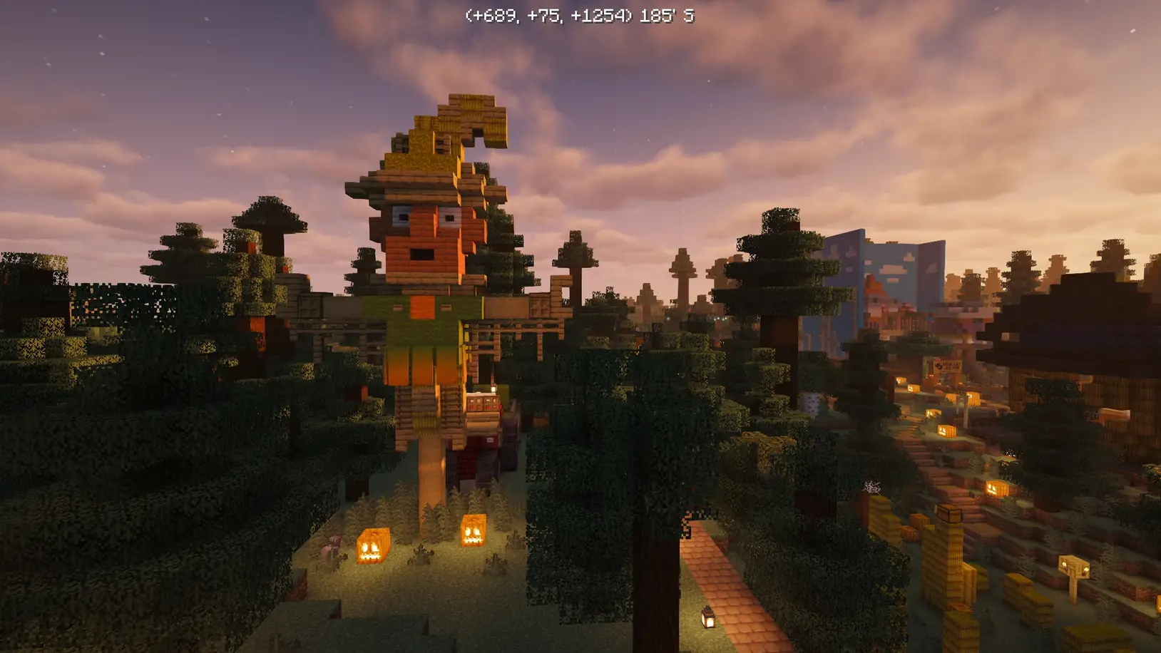A giant scarecrow above treetops and pumpkin-lit paths at the Fall Festival at sunset